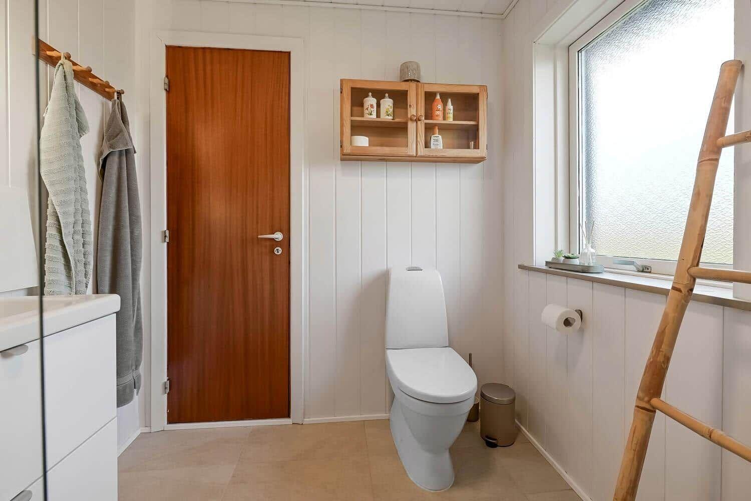 Bathroom with toilet, window, and wooden shelf on the wall.