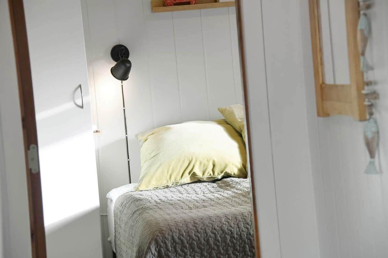 Bedroom with bed, pillows, and standing lamp against the wall.