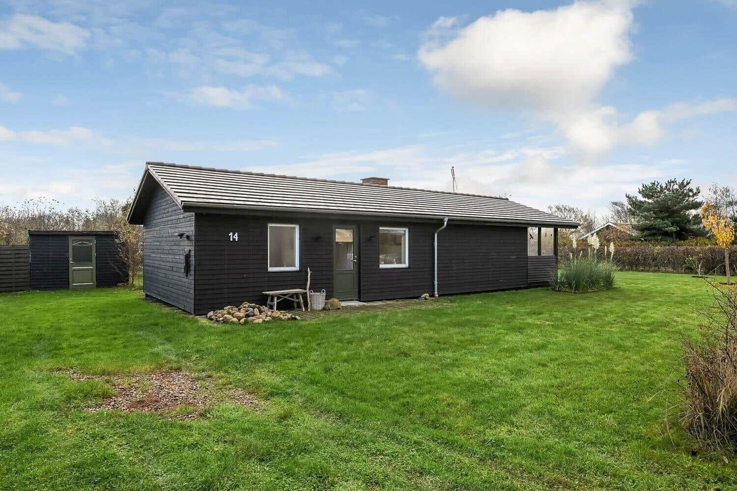 A dark wooden house with a green lawn and clear sky.