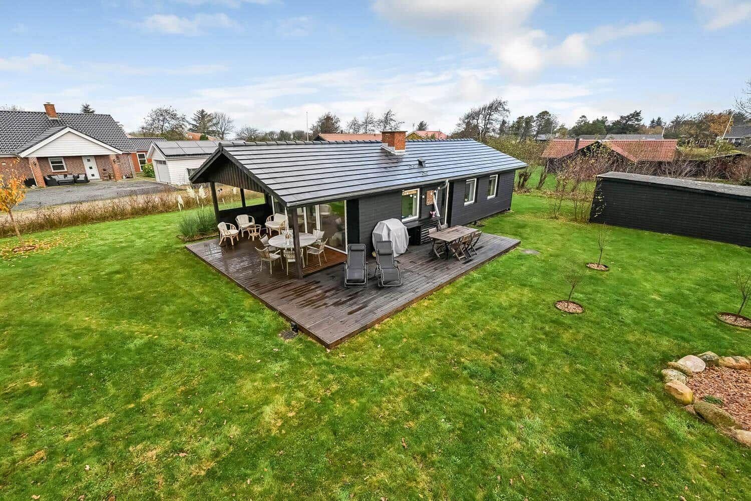 A house with terrace, garden, and garden furniture under blue sky.
