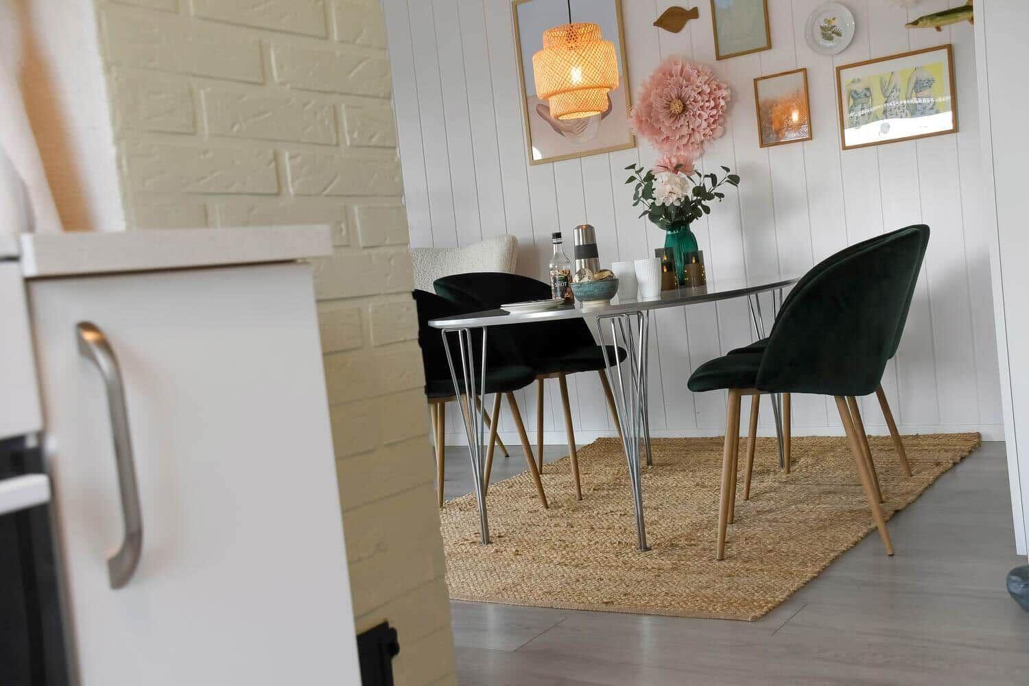 Dining table with four green chairs on rug against white wall.