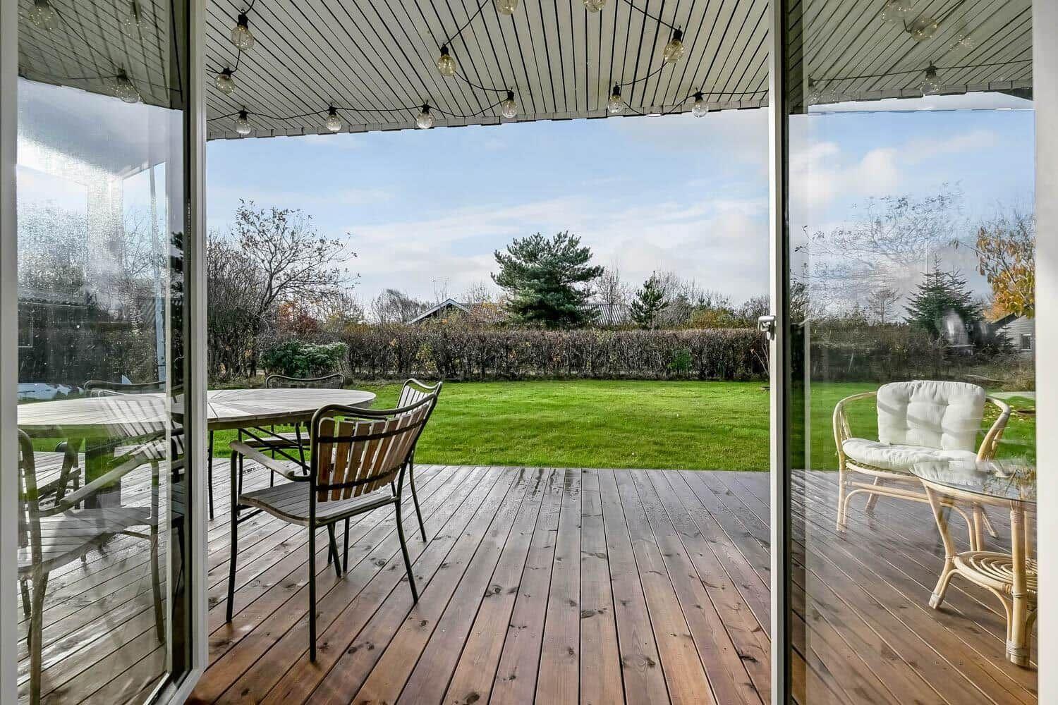 Deck with wooden planks, garden furniture, and string lights under roof