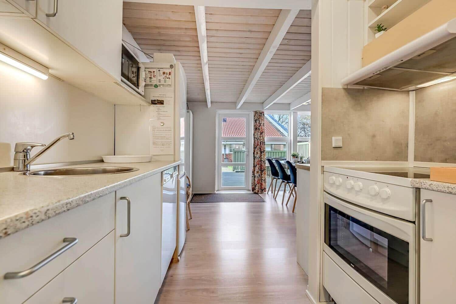 Kitchen with countertop, sink, and stove. Corridor to dining area with table and chairs.