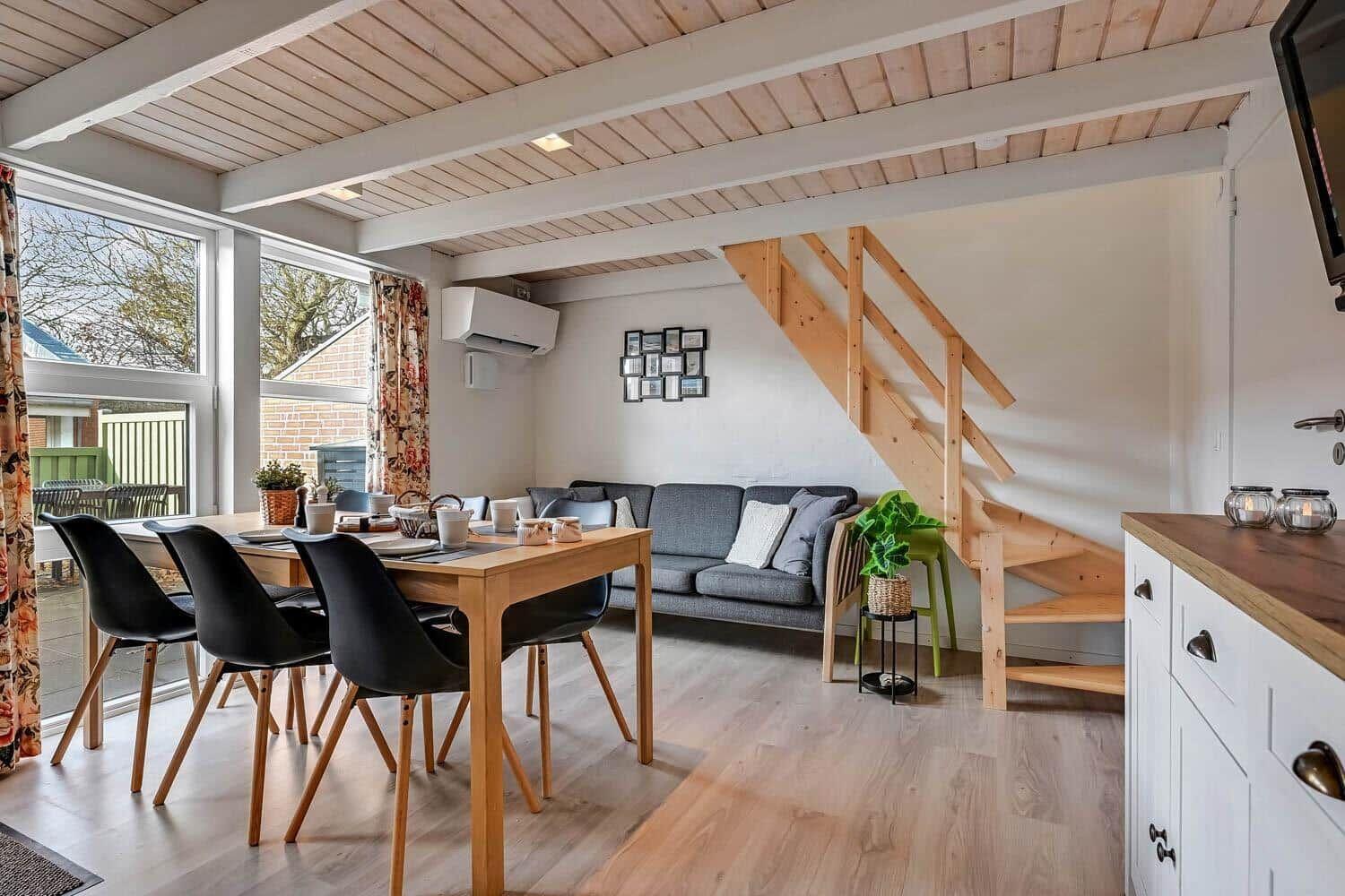 Dining area with table, chairs, and sofa. Wooden stairs lead upstairs.