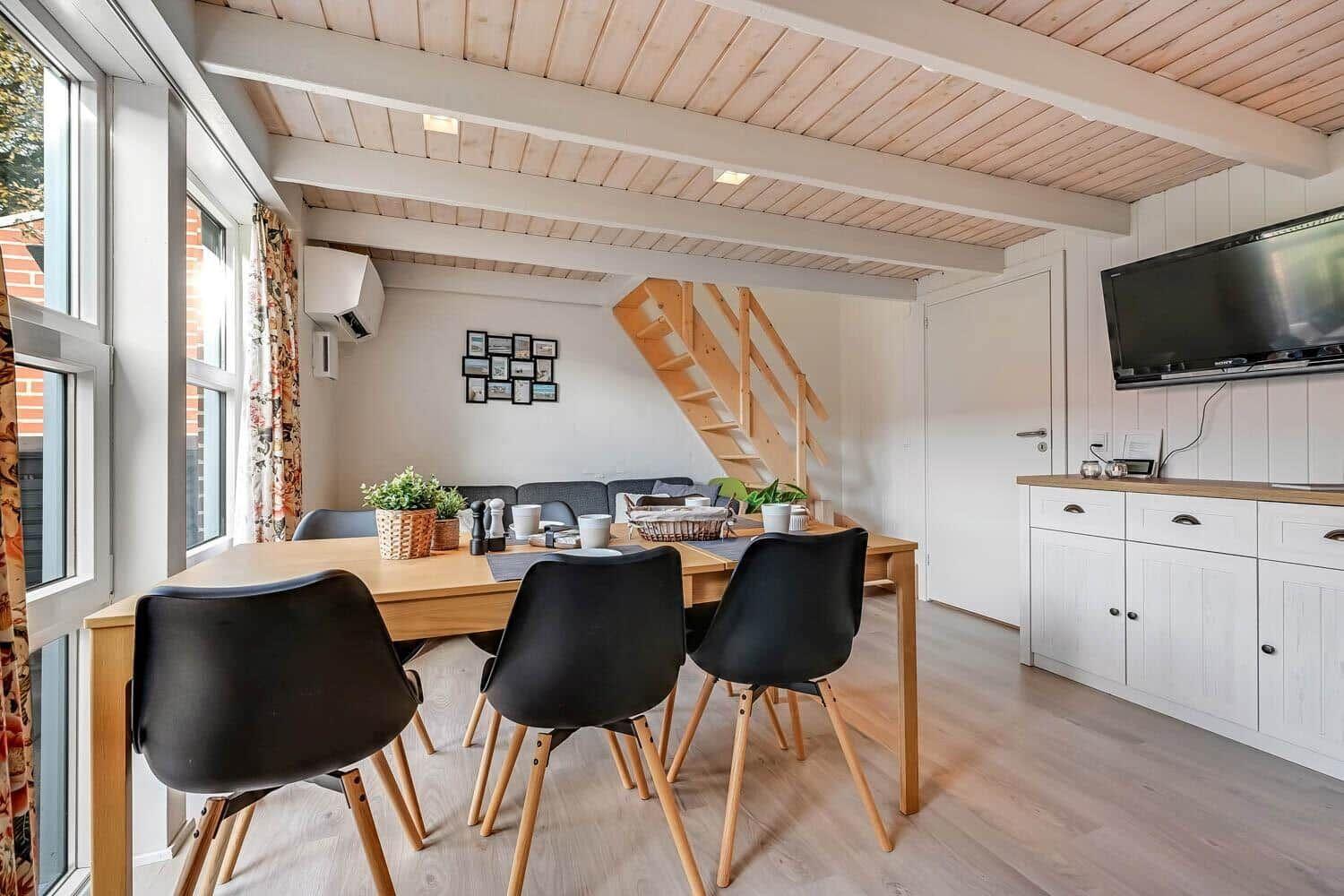 Dining area with table, chairs, and TV. Wooden ceiling and staircase visible.