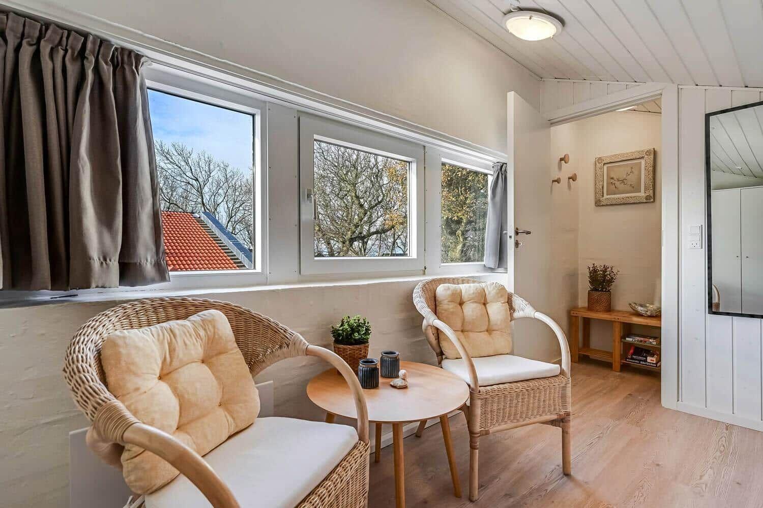 Two chairs and a table are placed in front of a window with a view of trees.