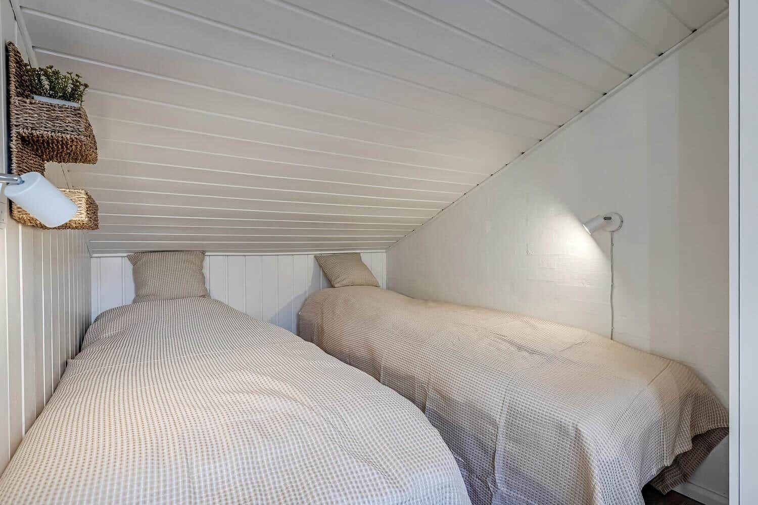 Two single beds under a sloped ceiling with wall lamps and plants.