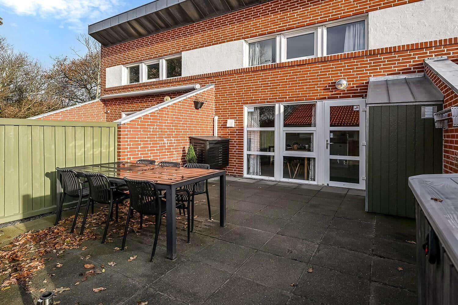 Backyard with table, chairs, and patio area. House with red brick and white windows.