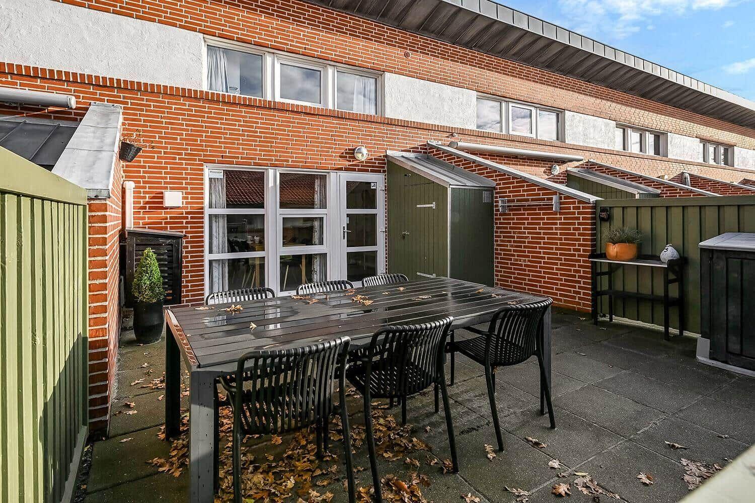 Terrace with table and chairs in front of brick house with windows and garden door.