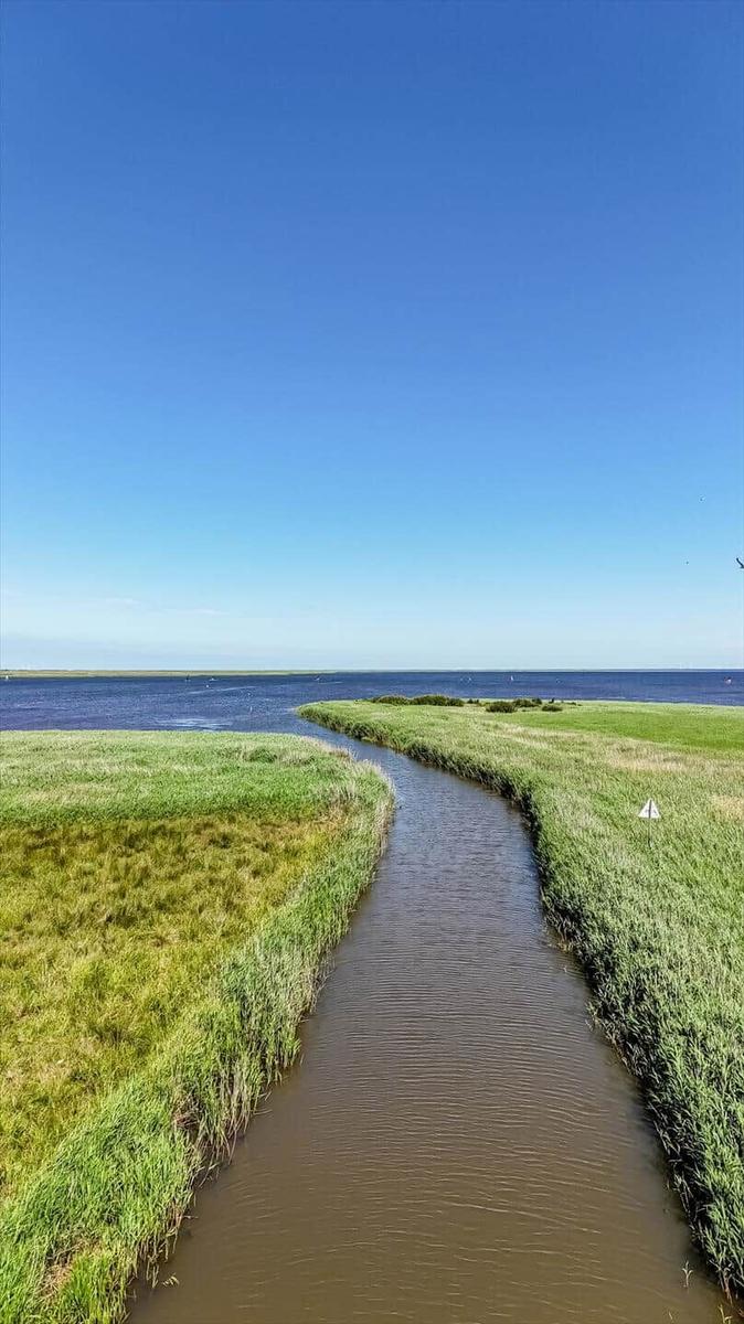 A narrow canal flows through green grass to a lake.