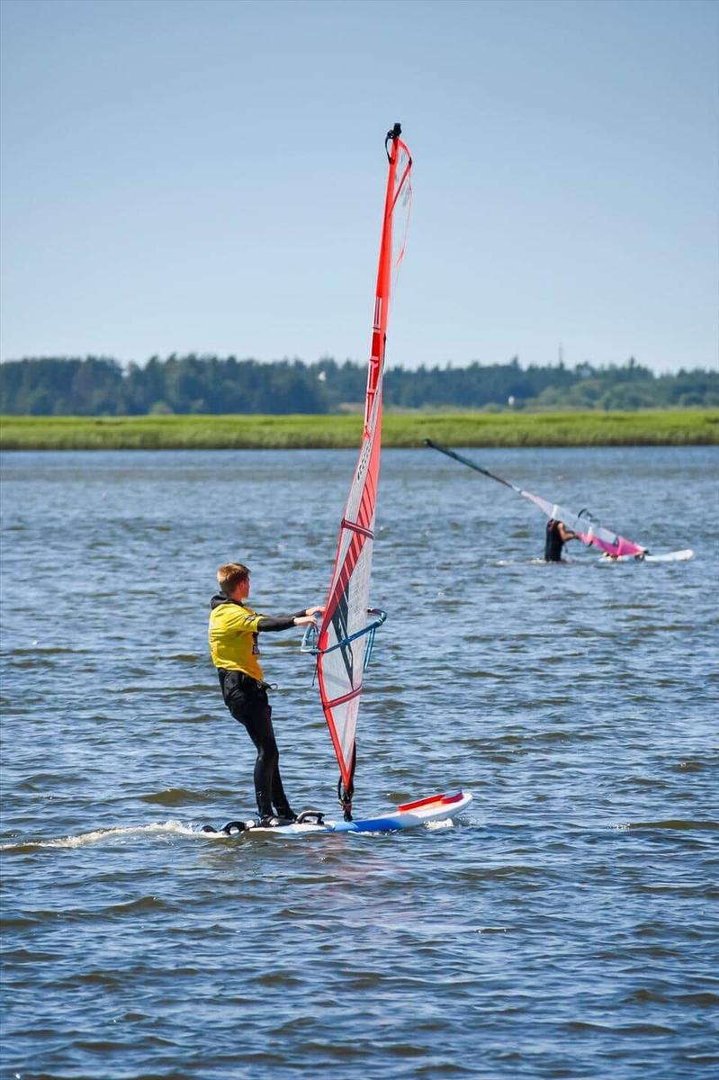 Windsurfer on water with red sail and another person in background.