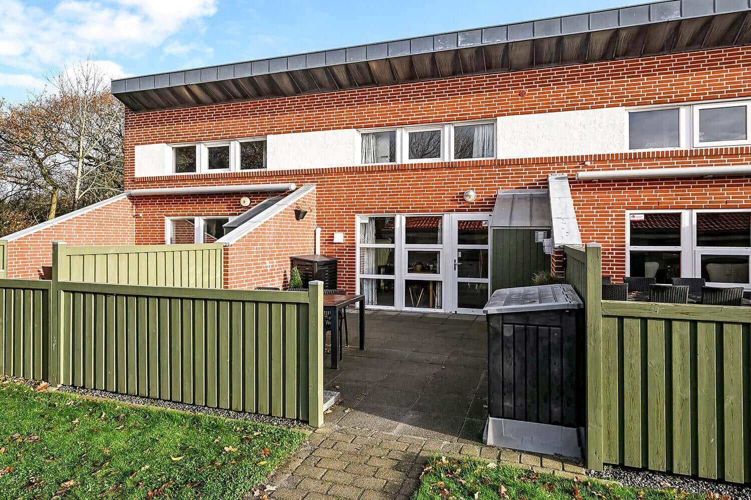 Red brick house with terrace and green fence.