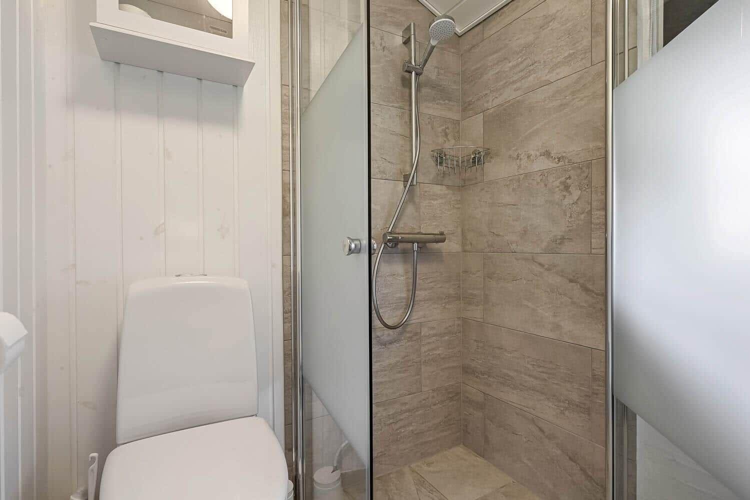 Bathroom with shower and toilet. Shower area with glass door and tiles.