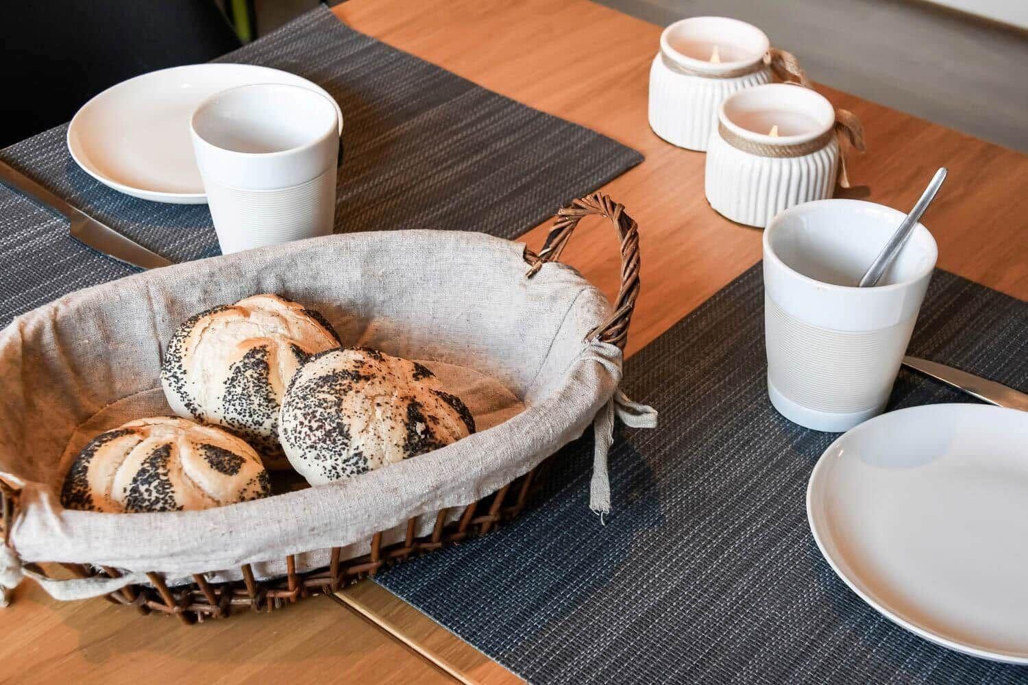 Breakfast table with bread basket, mugs, and candles.