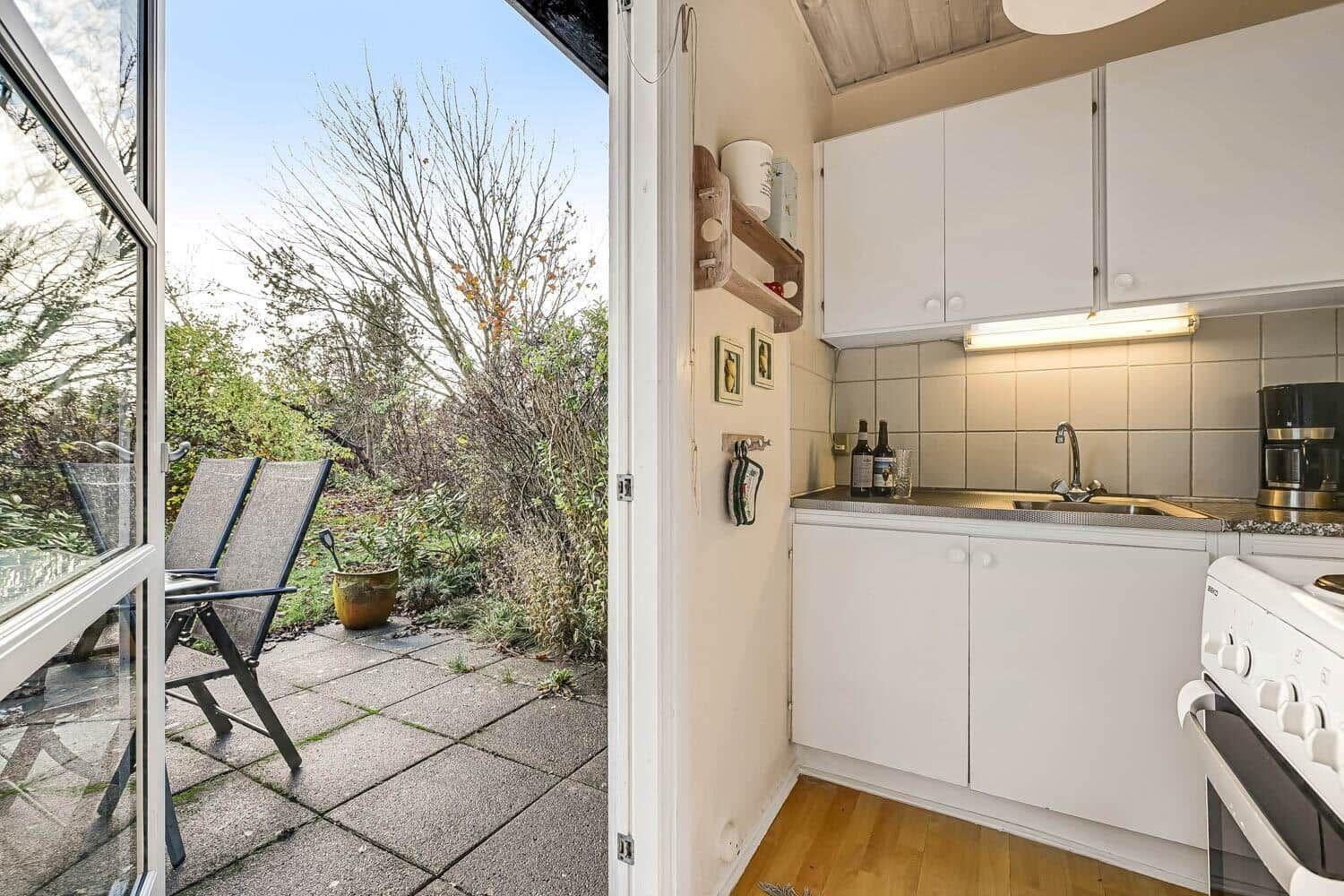 Kitchen with white cabinets and view of a paved balcony with chairs.