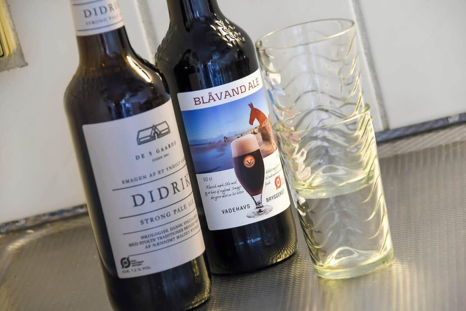 Two beer bottles and a glass are on a metal surface.