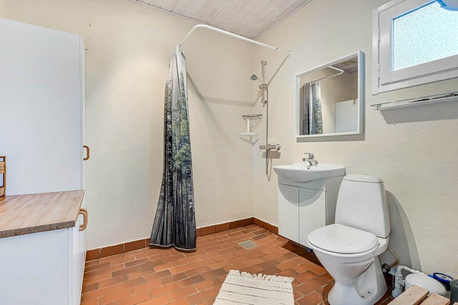 Bathroom with shower, sink and toilet. Terracotta floor and window.