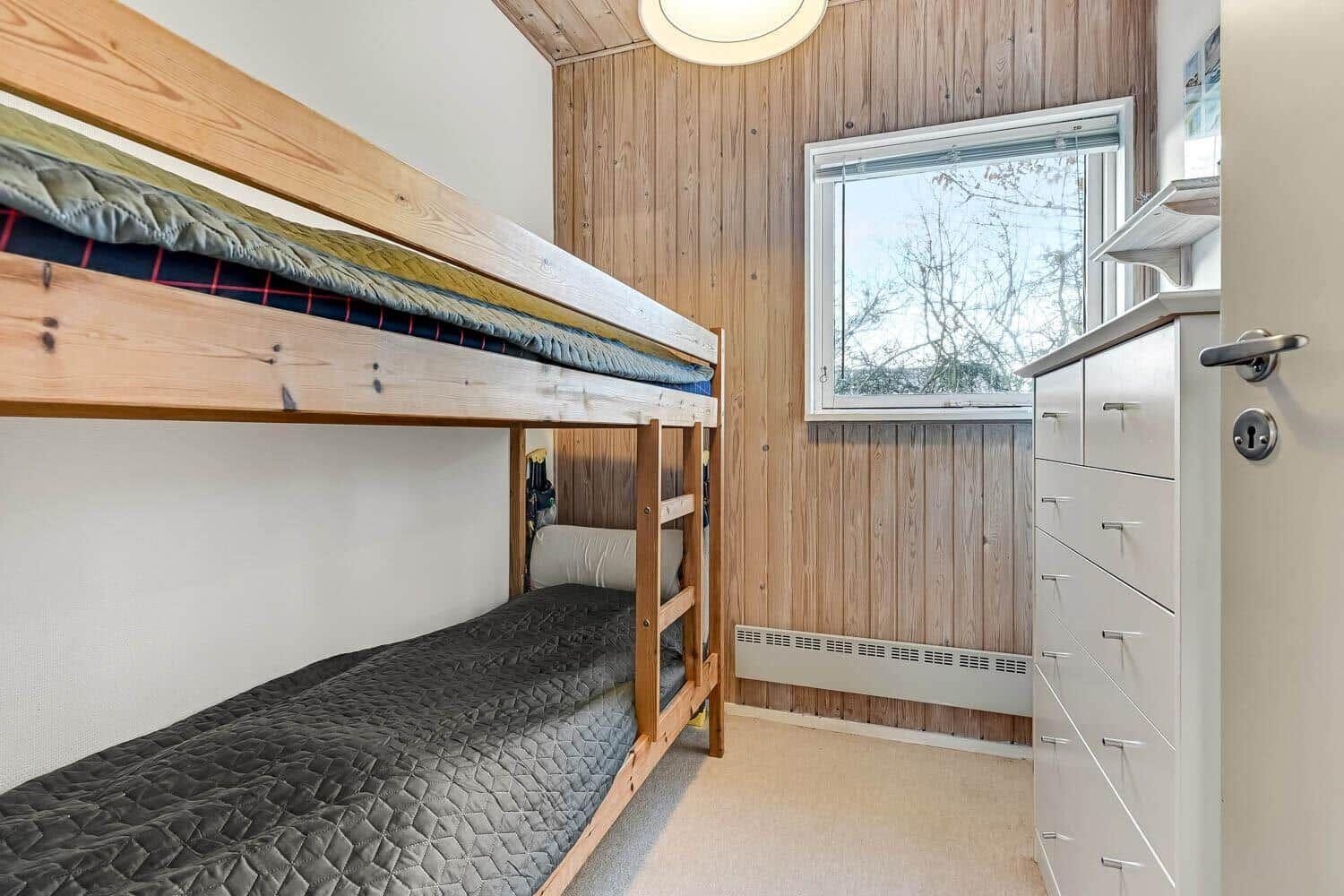Room with bunk bed, wood wall, and window.