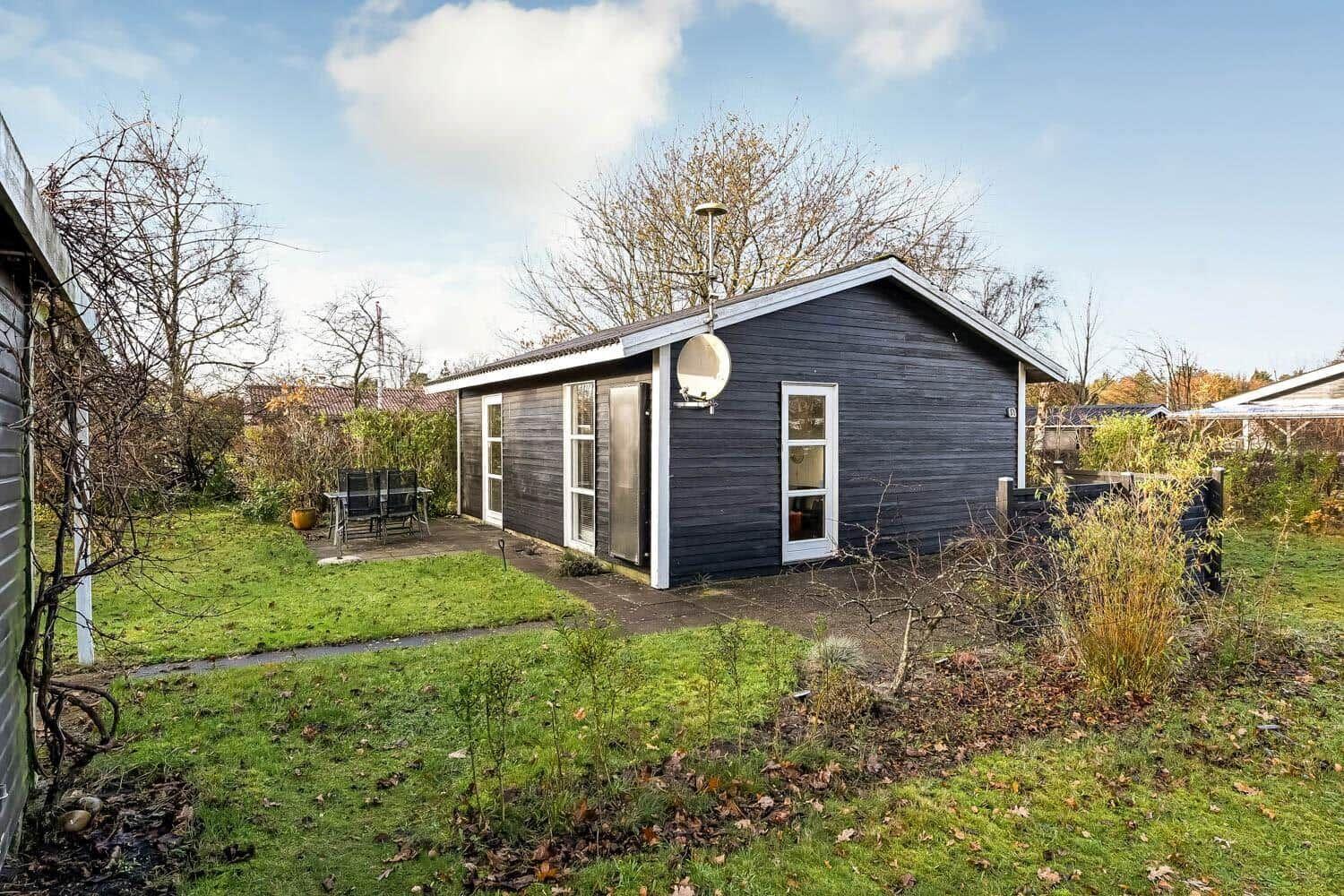 Black wooden house with garden and terrace. Satellite dish and windows visible.