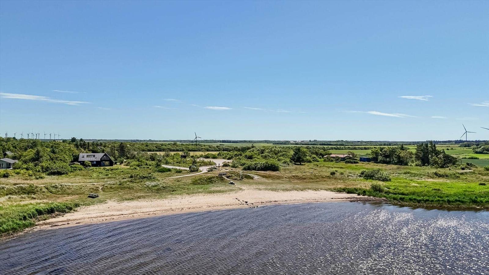 House by the water with view of wind turbines and green landscape.