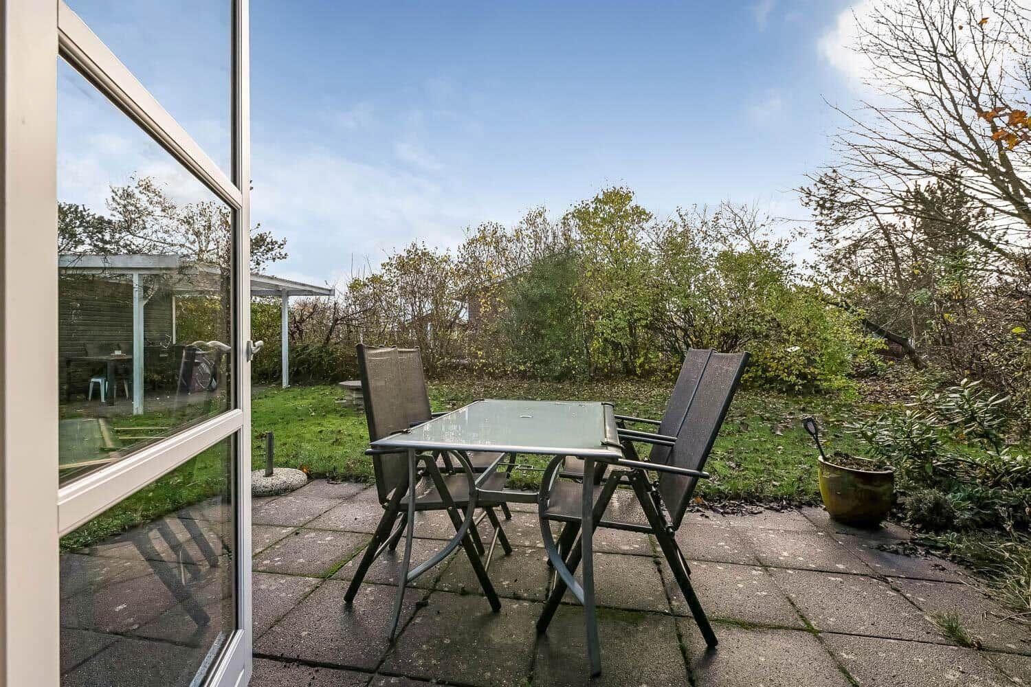 Terrace with table and two chairs, view of a green garden with trees.