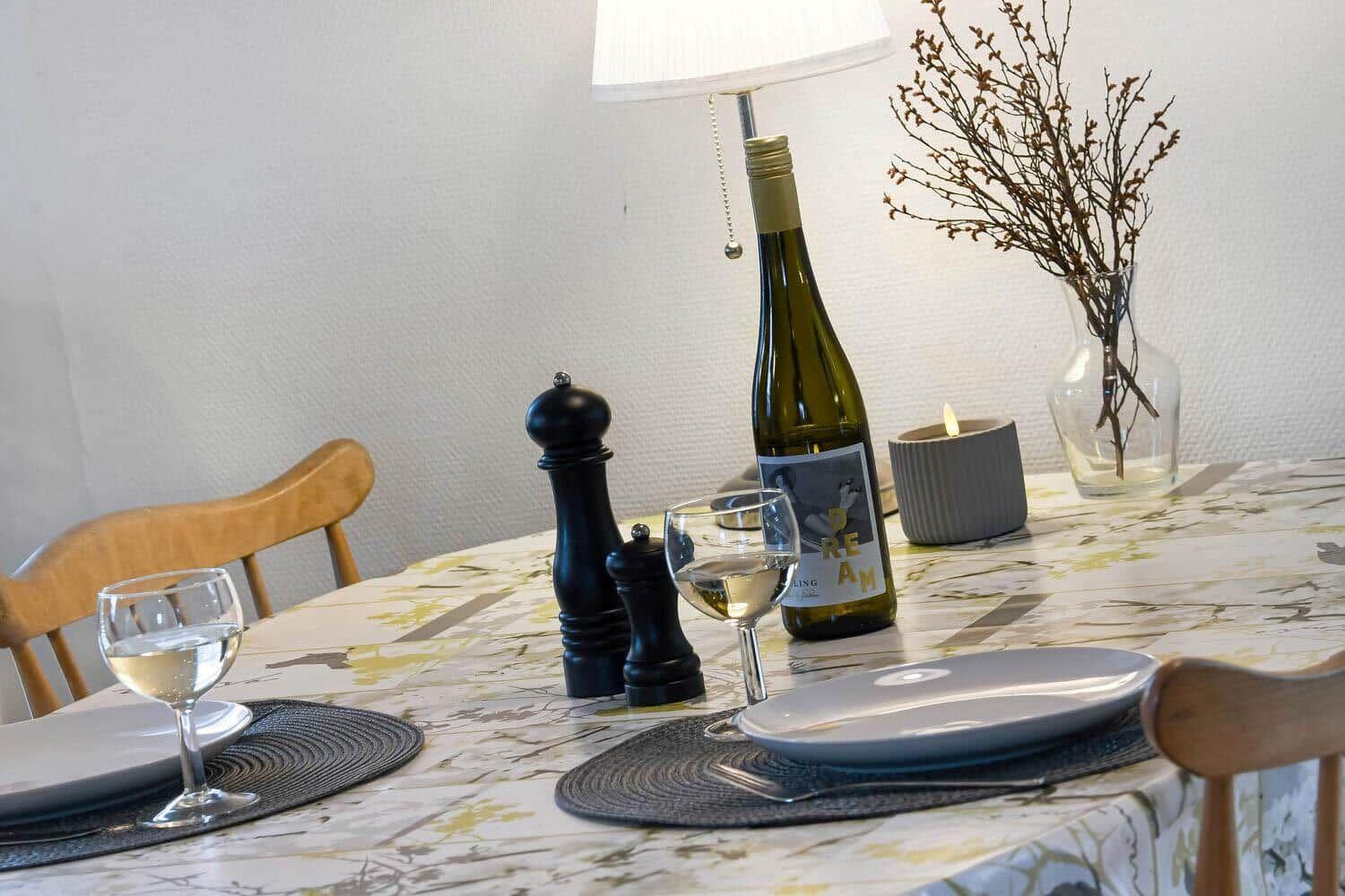 Dining table set for two, wine bottle, glasses, and decor.
