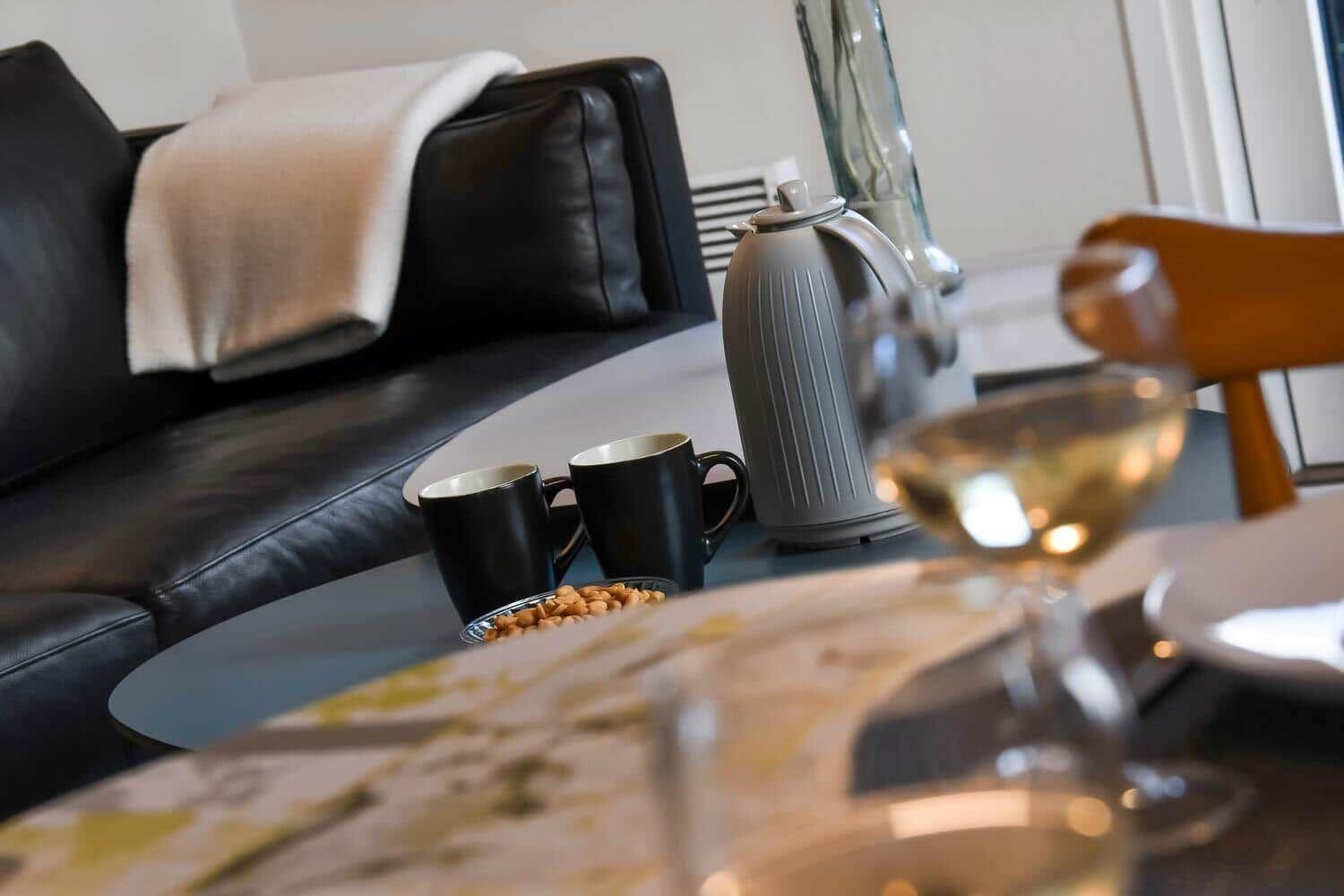 Black leather sofa with blanket, table with coffee mugs and kettle.