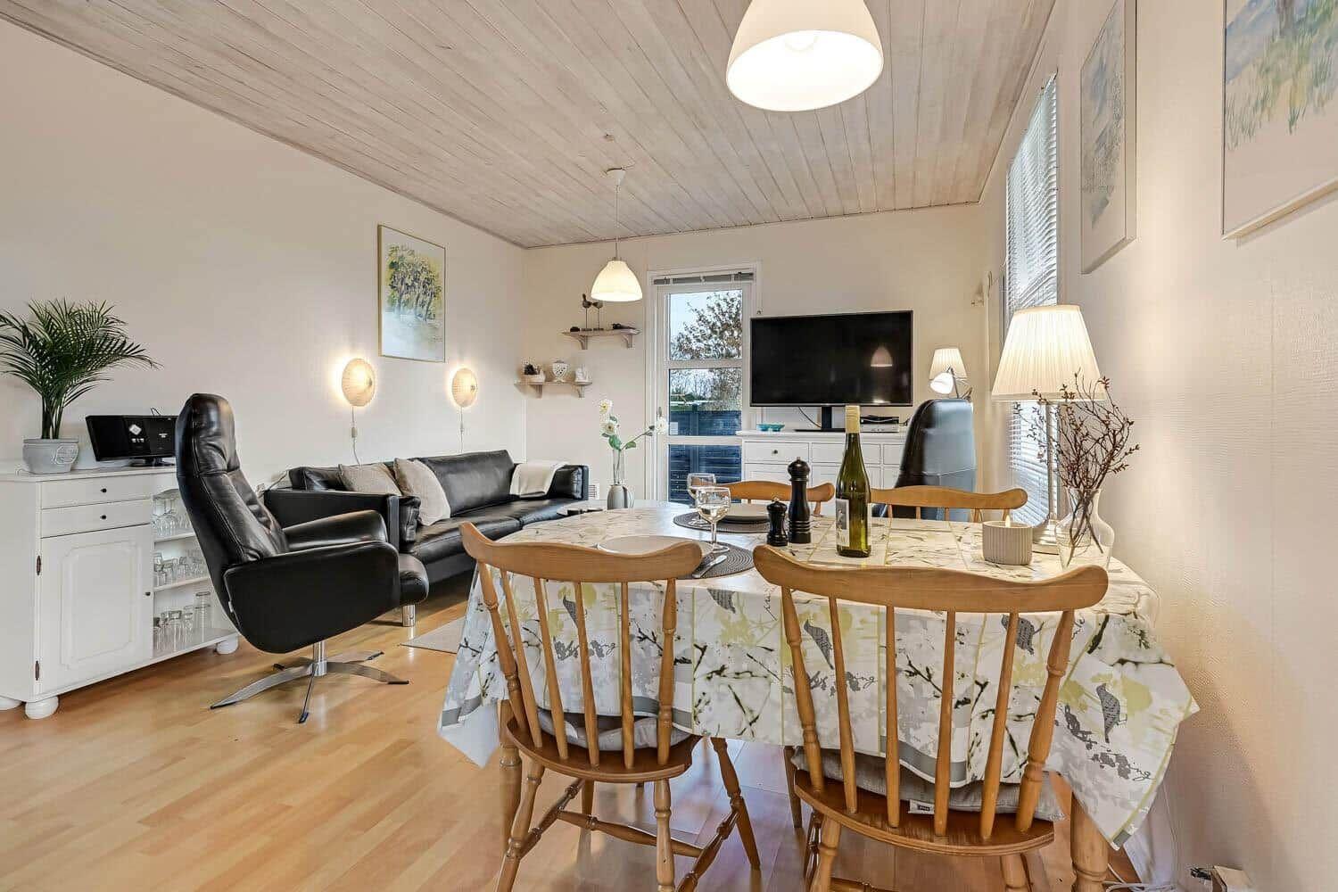 Dining area with wooden table and chairs, living area with sofa and TV.