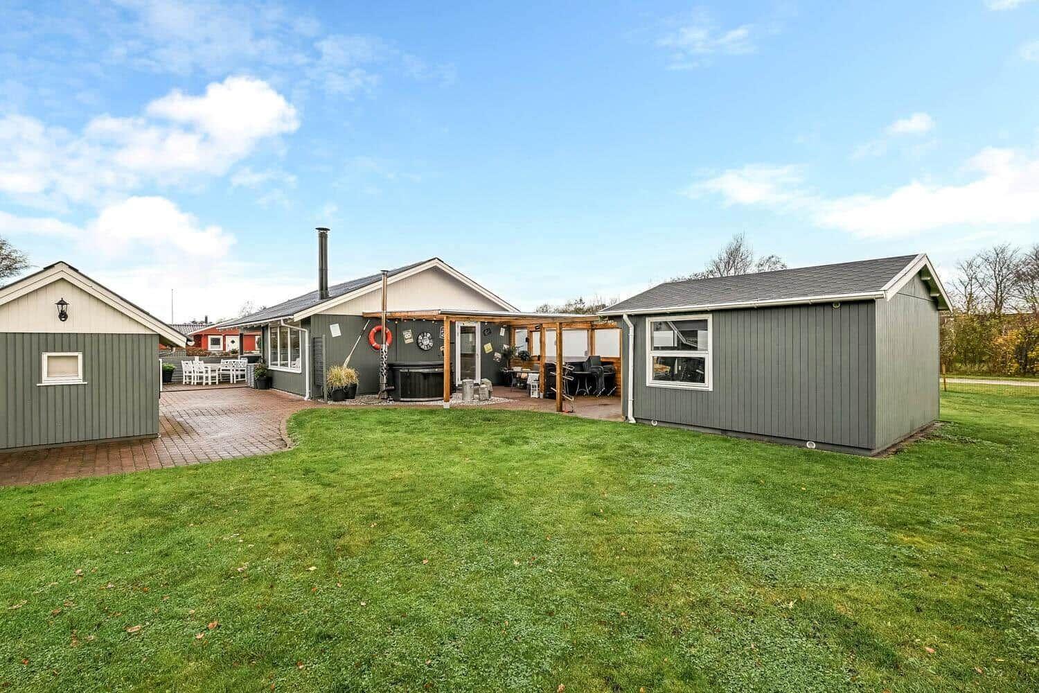 House with garden, terrace, and hot tub. Left utility building. Background with trees.