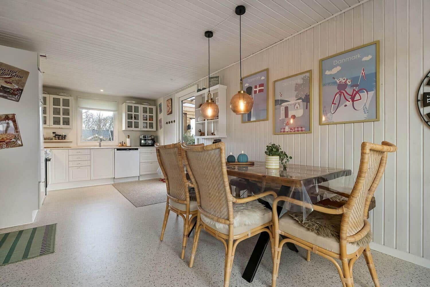 Dining room with table and chairs, kitchen area in background, wall art with Denmark motifs.