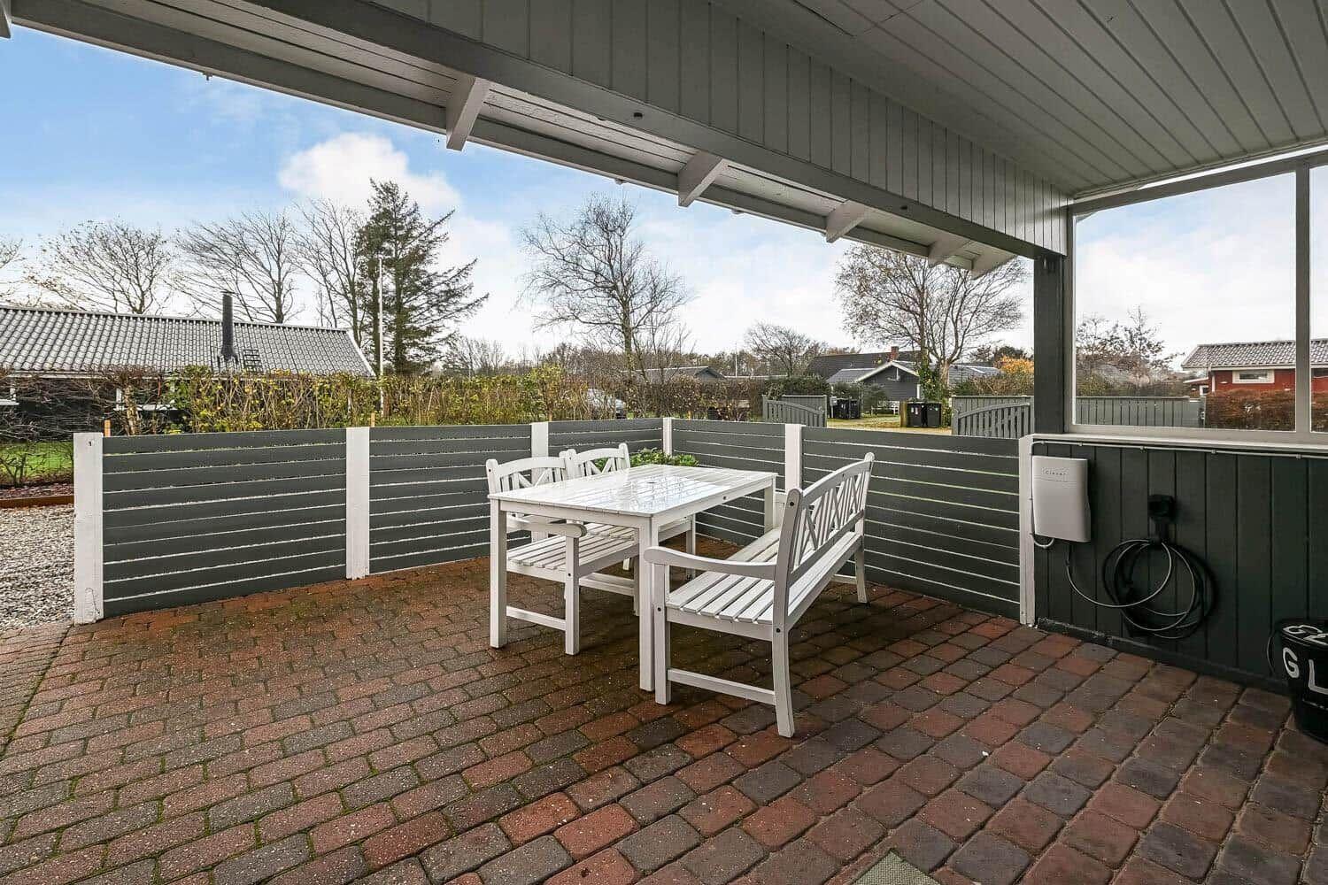 Terrace with white table and benches, bordered by gray fence and red bricks.
