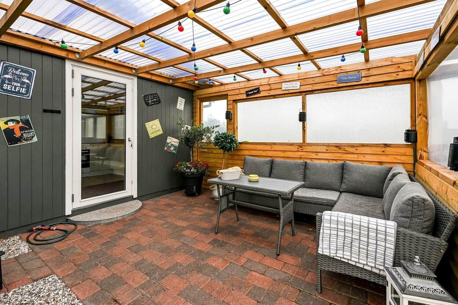 Terrace with seating group, table, and string lights under glass roof.