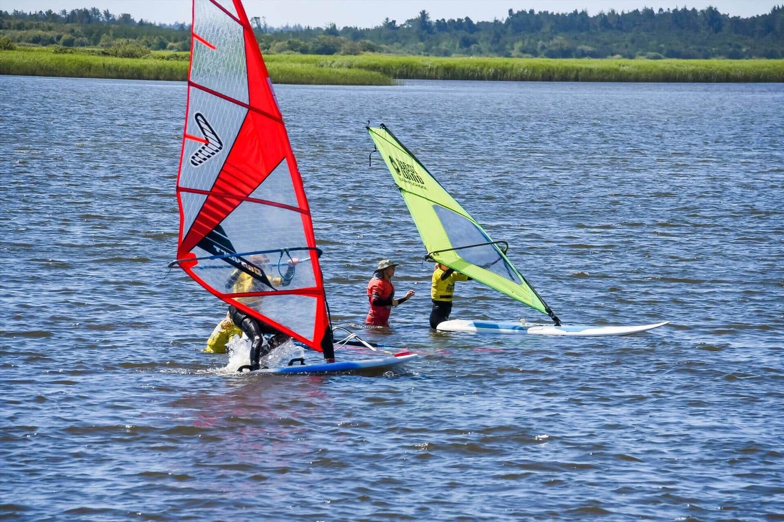 Two windsurfers practice on the water with colorful sails.