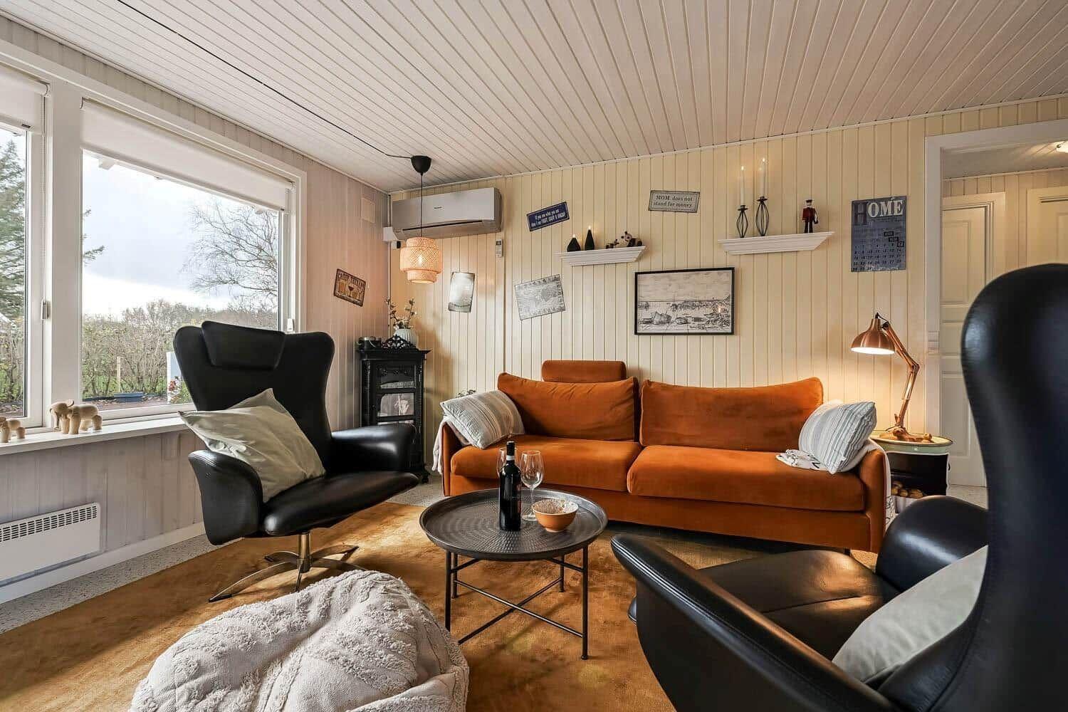 Living room with orange sofa, black chairs, and wood-paneled walls.