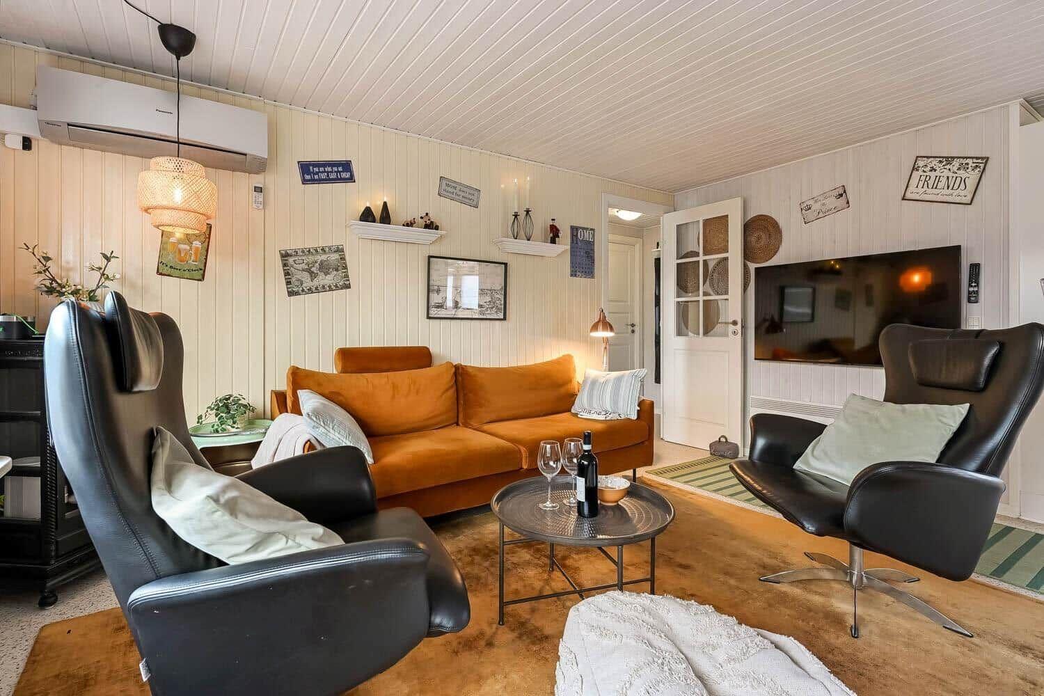 Living room with orange sofa, two black chairs, and TV mounted on the wall.