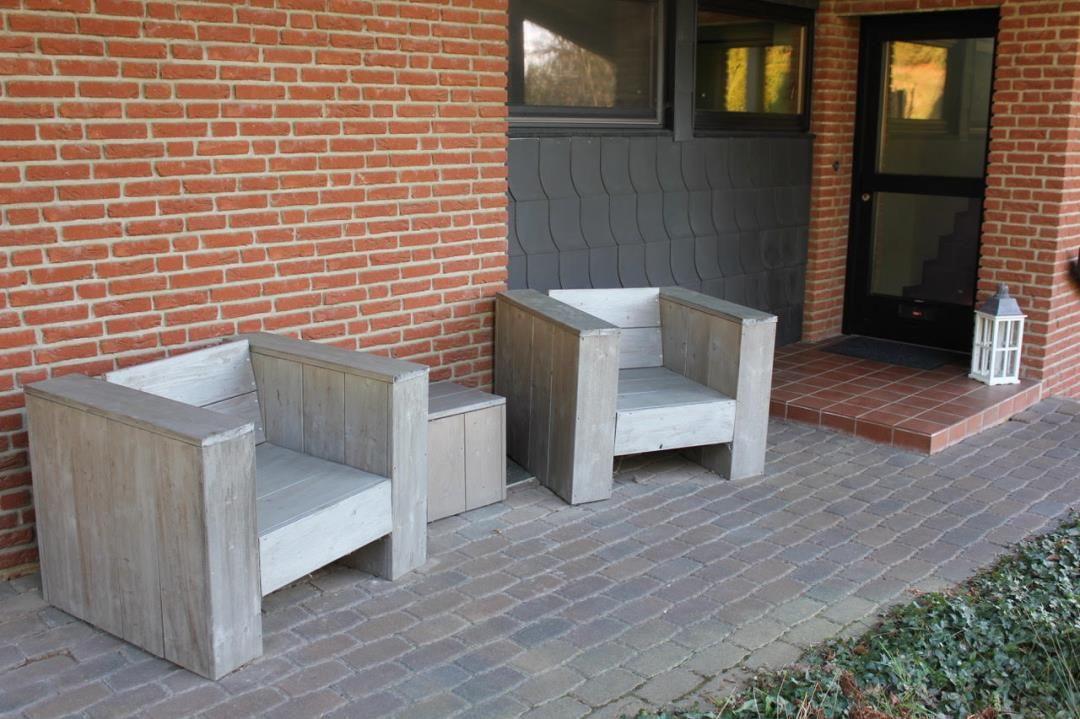 Zwei hölzerne Sitzgelegenheiten stehen auf einem gepflasterten Hof vor einer Backsteinmauer.