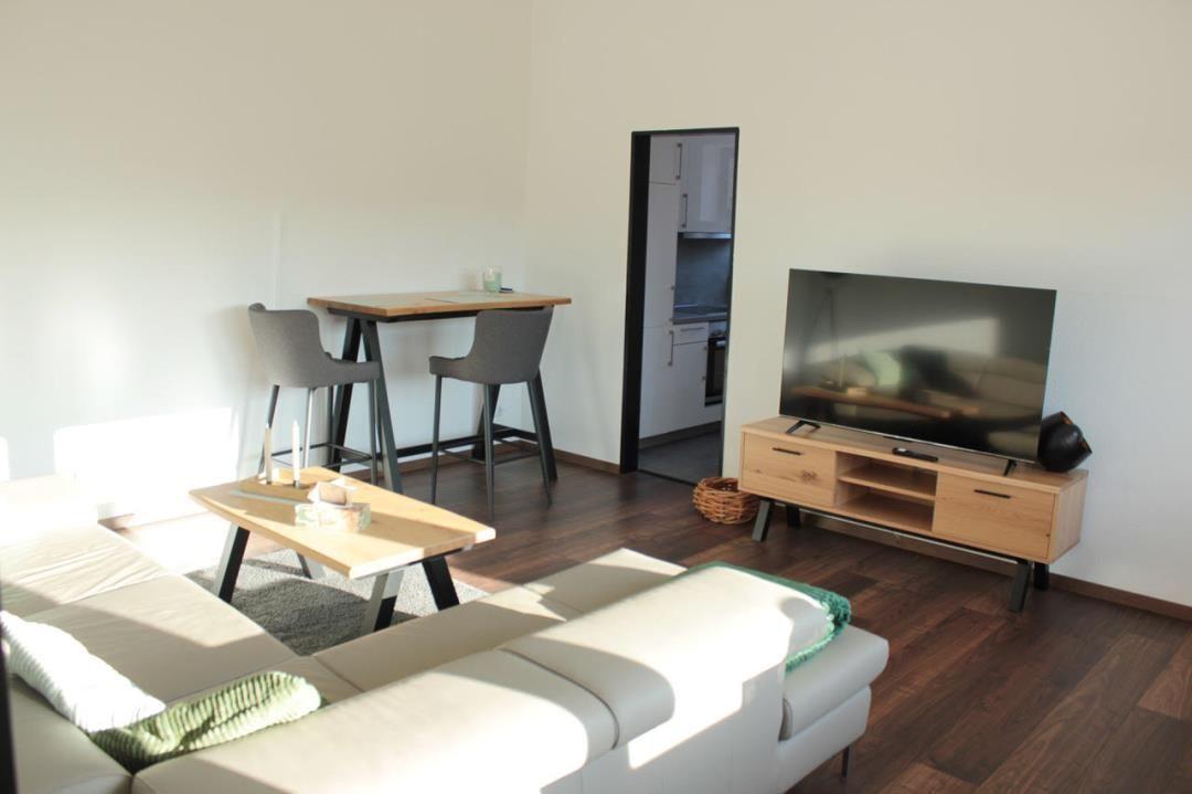 Wohnzimmer mit Sofa, TV und Essbereich. Küche im Hintergrund sichtbar.