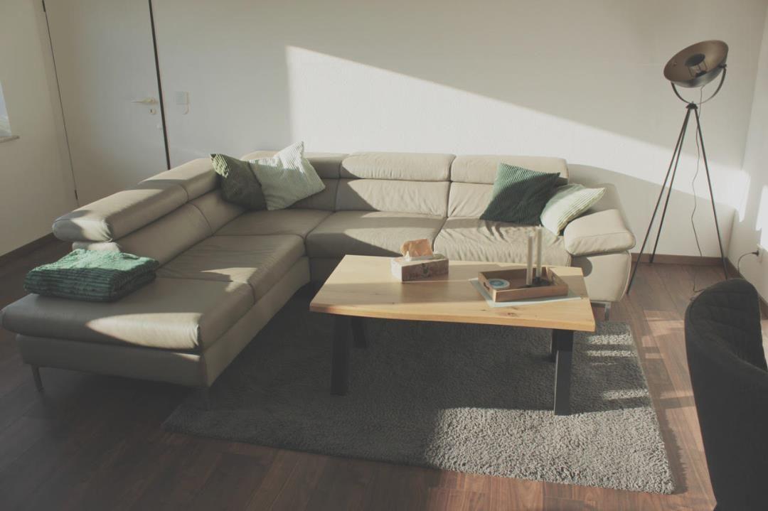 Ein Wohnzimmer mit Ecksofa, Holztisch und Stehlampe.