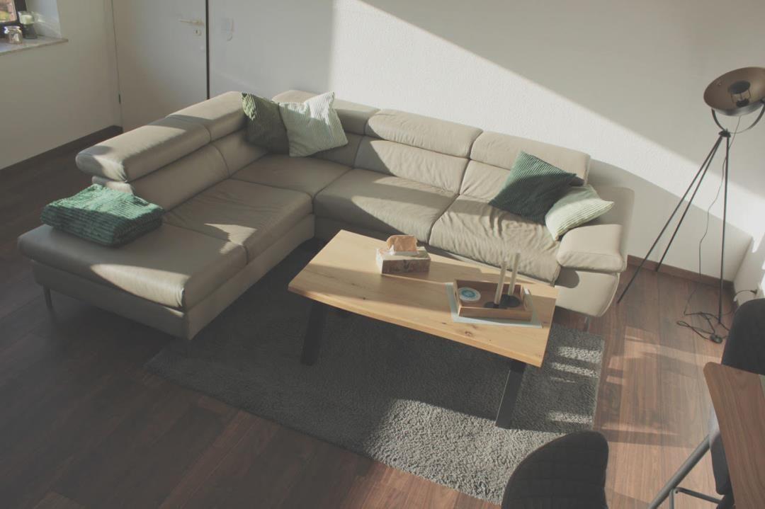 Ein Wohnzimmer mit L-förmigem Sofa, Holztisch und Stehlampe.
