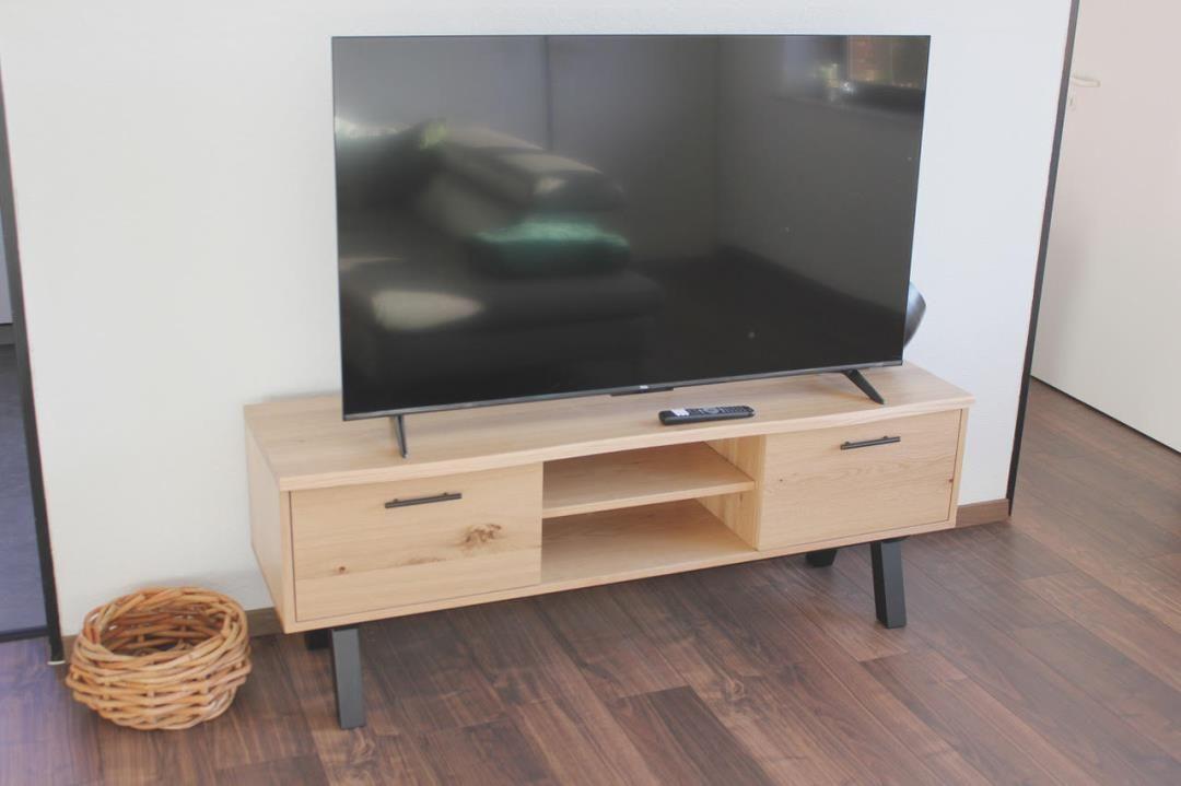 Flachbild-TV auf Holz-TV-Board mit Schubladen und offener Ablagefläche.