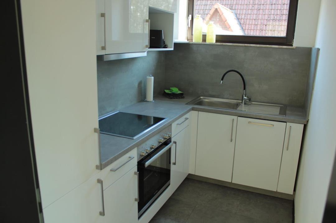 Küche mit weißen Schränken, Edelstahlspüle und Fenster mit Blick auf Dach