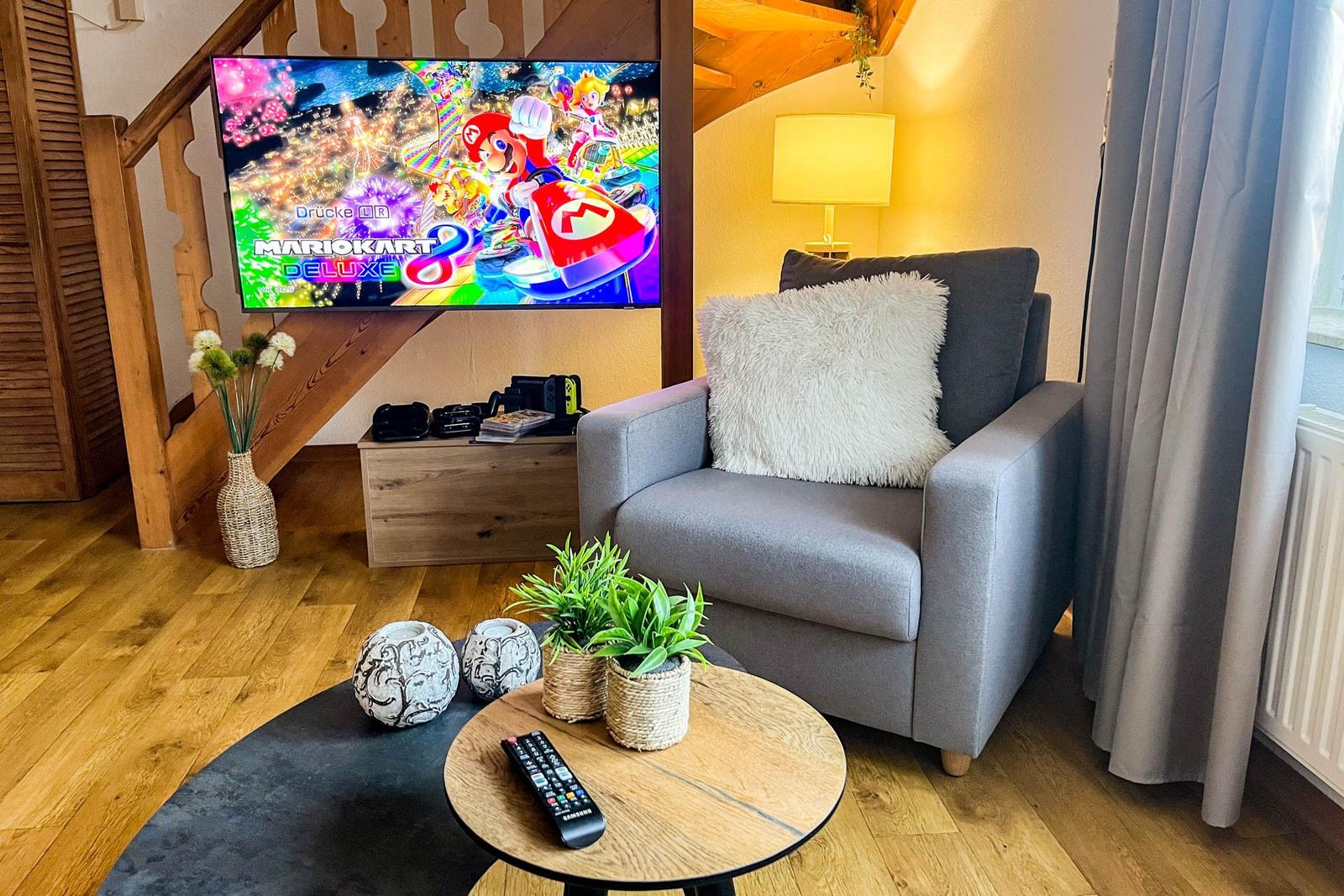 Wohnzimmer mit Sessel, Fernseher und Holzboden.