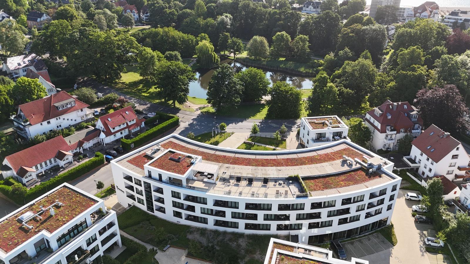 Modernes Gebäude mit begrüntem Dach und umliegenden Häusern in grüner Umgebung.