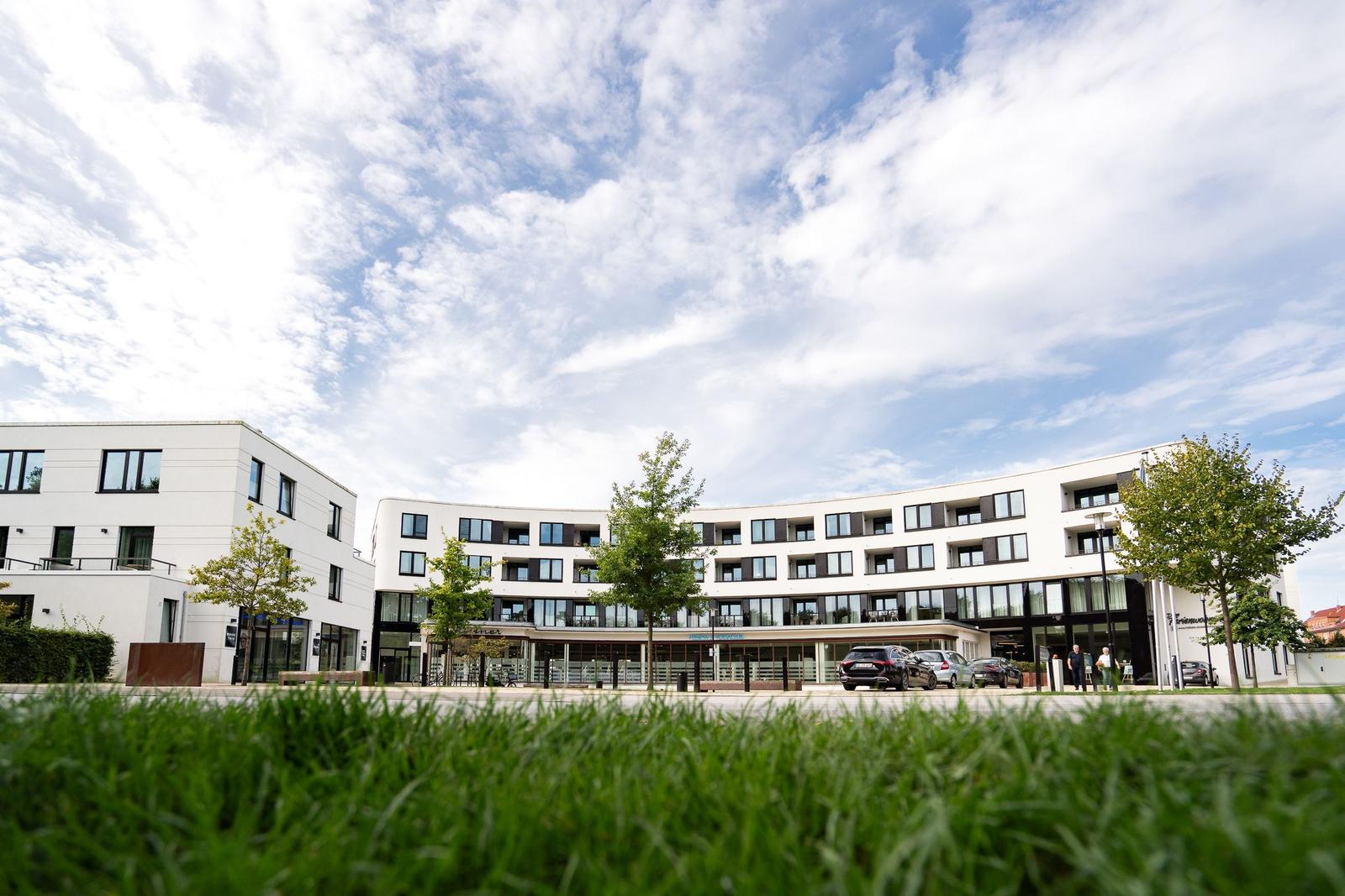 Moderne Wohngebäude mit Parkplatz und Grünflächen unter blauem Himmel.