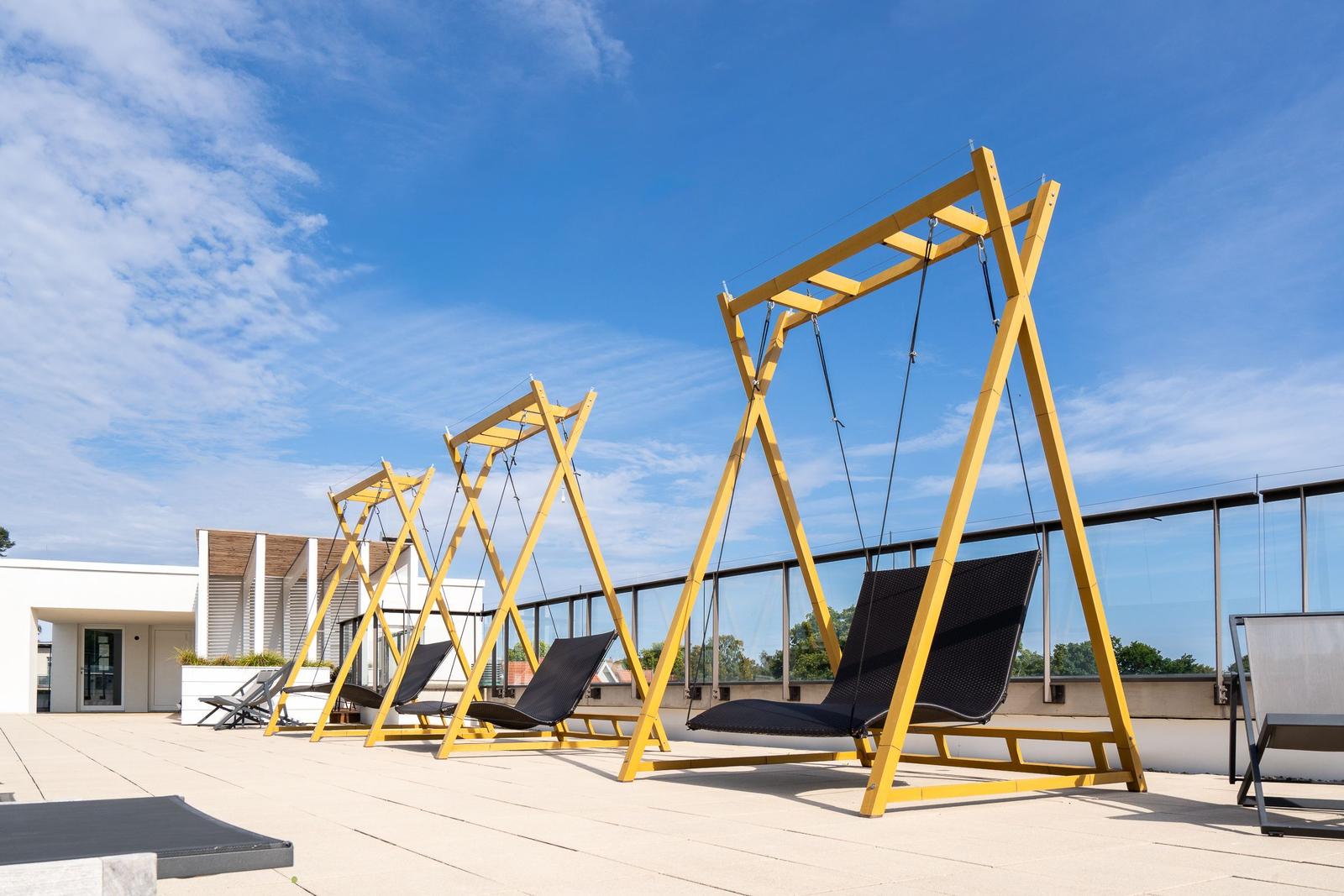 Drei gelbe Schaukelstühle auf einer Terrasse unter blauem Himmel.