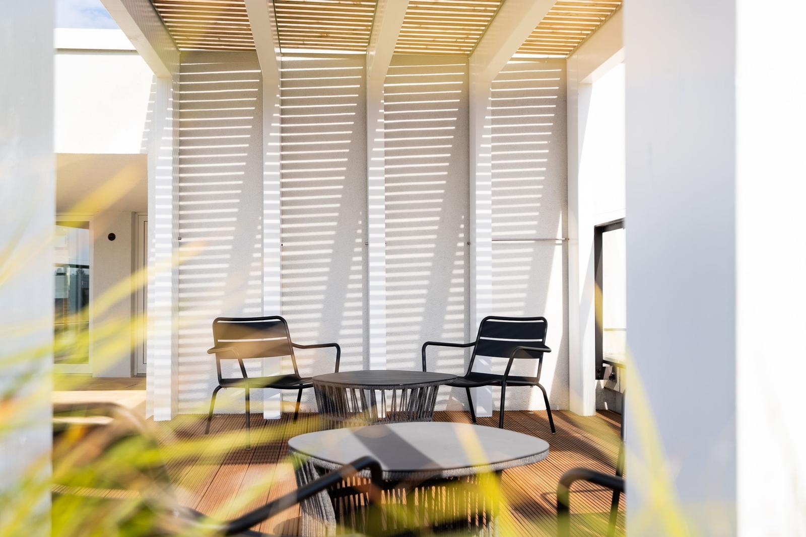 Terrasse mit zwei Stühlen und Tisch unter Holzüberdachung.