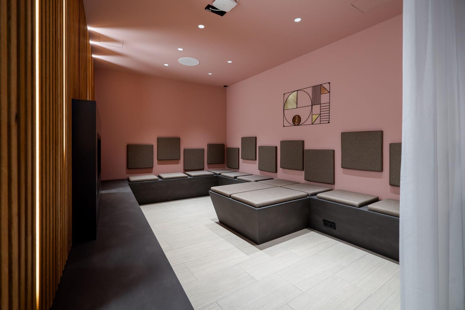 Raum mit Sitzbänken an rosa Wänden und geometrischer Wanddekoration.