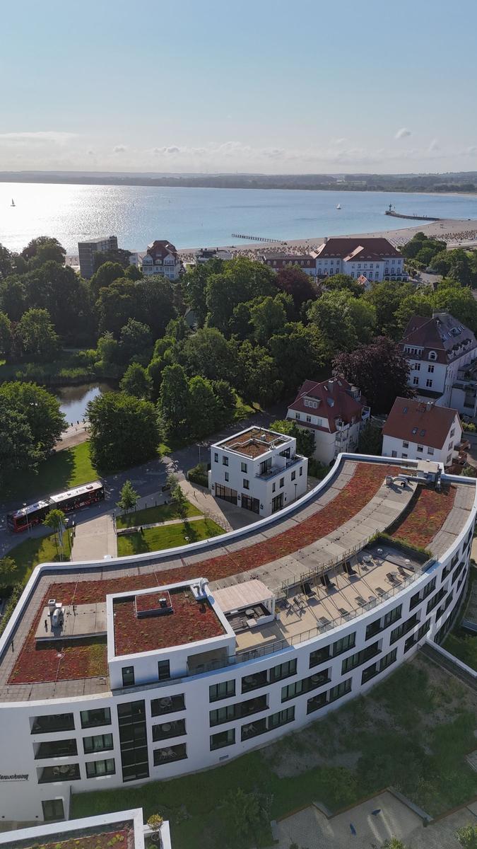 Modernes Gebäude mit begrüntem Dach und Blick auf Strand und See.