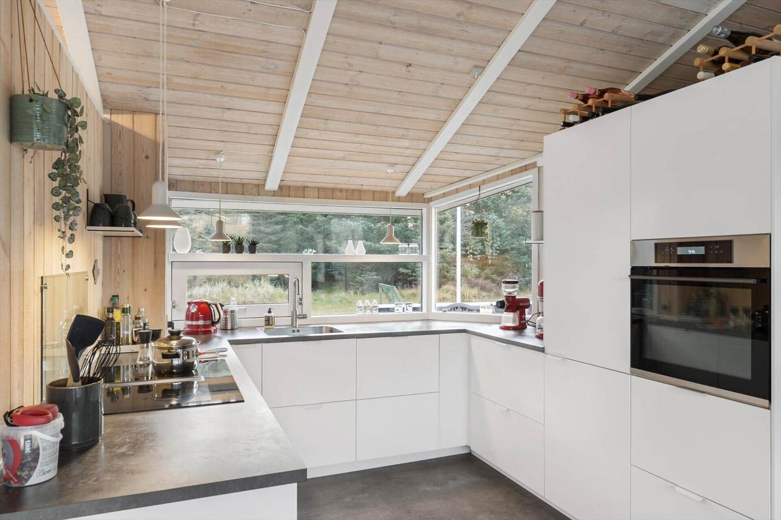 Kitchen with white cabinets, wooden ceiling, and large windows to the forest.