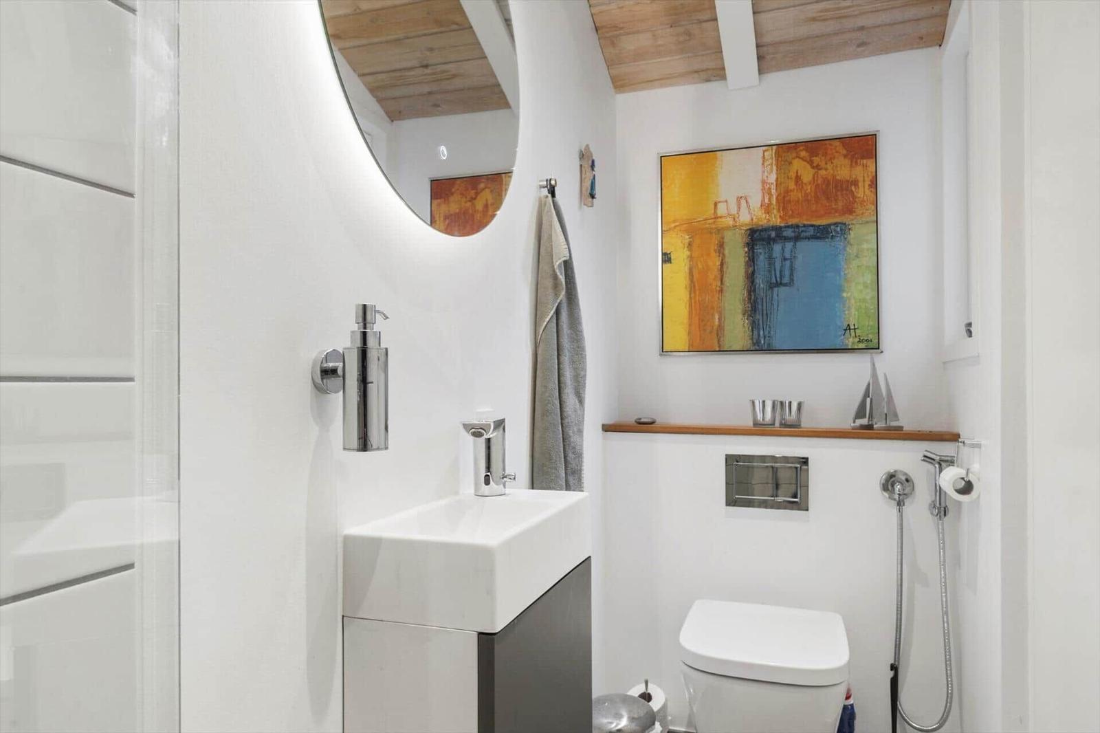 Bathroom with sink, toilet, and shower. Wall art and wooden ceiling.